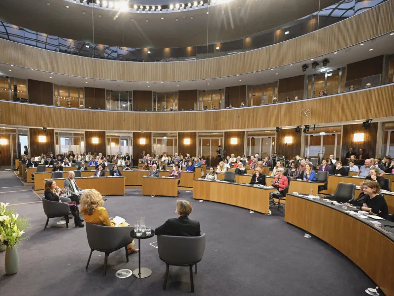 Teilnehmer:innen der Podiumsdiskussion von hinten, Blick Richtung Veranstaltungsteilnehmer:innen